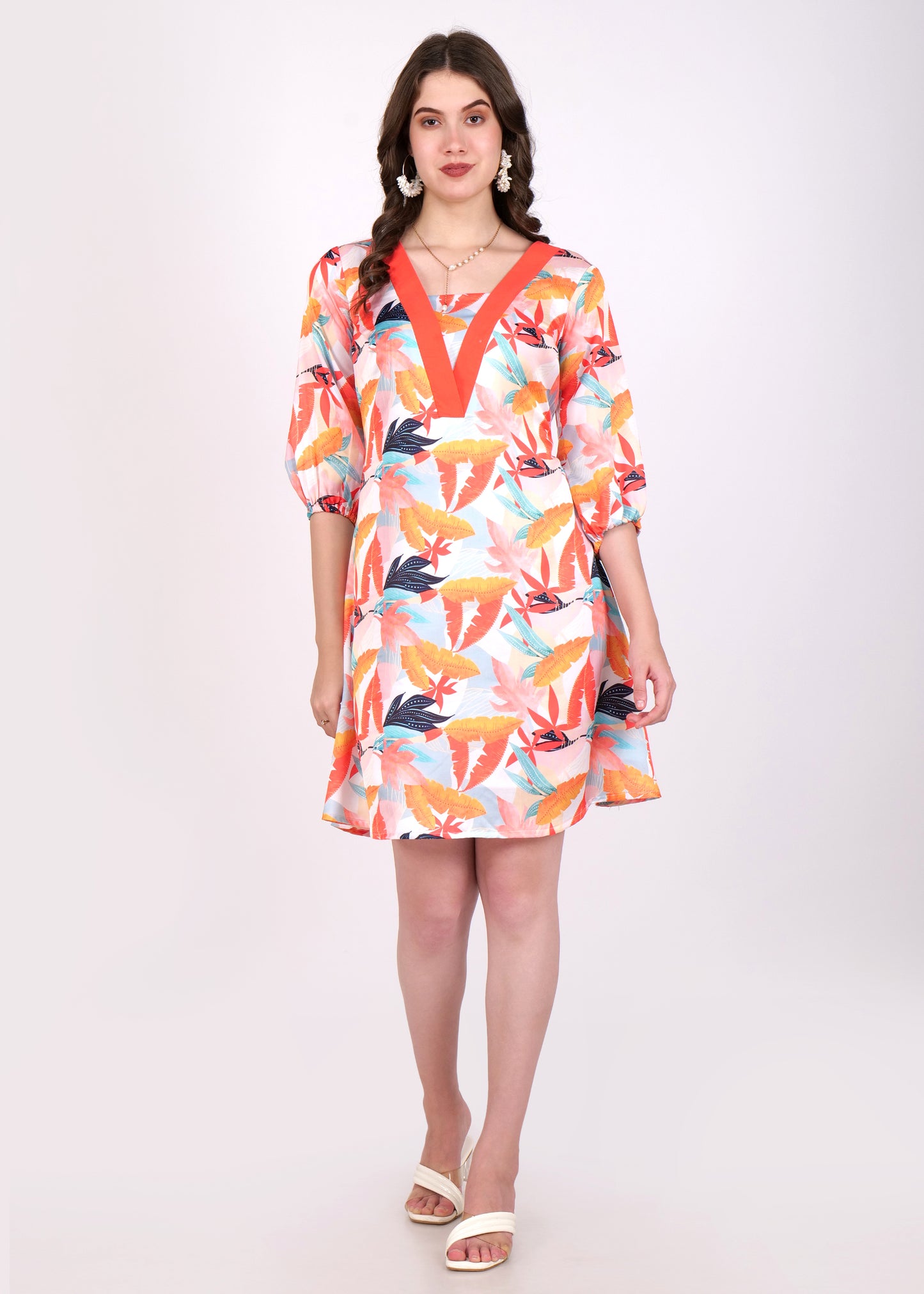 A woman wearing a colorful floral-print V-neck dress with a bold orange border. The dress has three-quarter sleeves and a flowing A-line cut