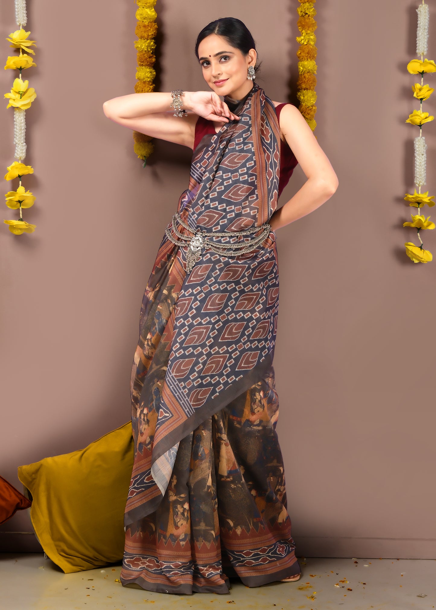 A woman in a traditional brown and earthy tone Ikat printed saree, styled with intricate silver jewelry