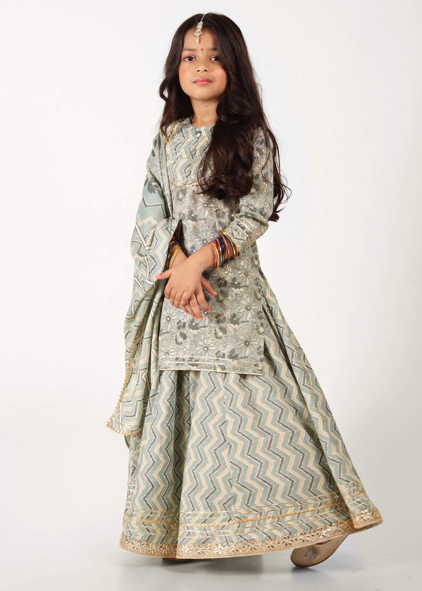 "A young girl wearing a light green embroidered ethnic kurta with zigzag patterned palazzo and matching dupatta, posing confidently."
