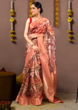 Model draped in a peach-colored saree featuring intricate cityscape artwork with gold zari detailing