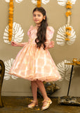 Little girl in a peach and gold puff sleeve dress with intricate golden checkered patterns, posing with elegance and grace in a festive setup.