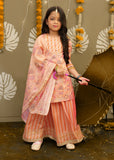A young girl is wearing a peach-colored floral ethnic outfit featuring a flowy skirt and dupatta, accessorized with bangles, and holding a brown traditional umbrella.