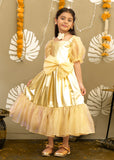A young girl in a shimmering golden gown with puffed sleeves, a large bow at the waist, and delicate accessories, standing in a festive setting decorated with marigold flowers.