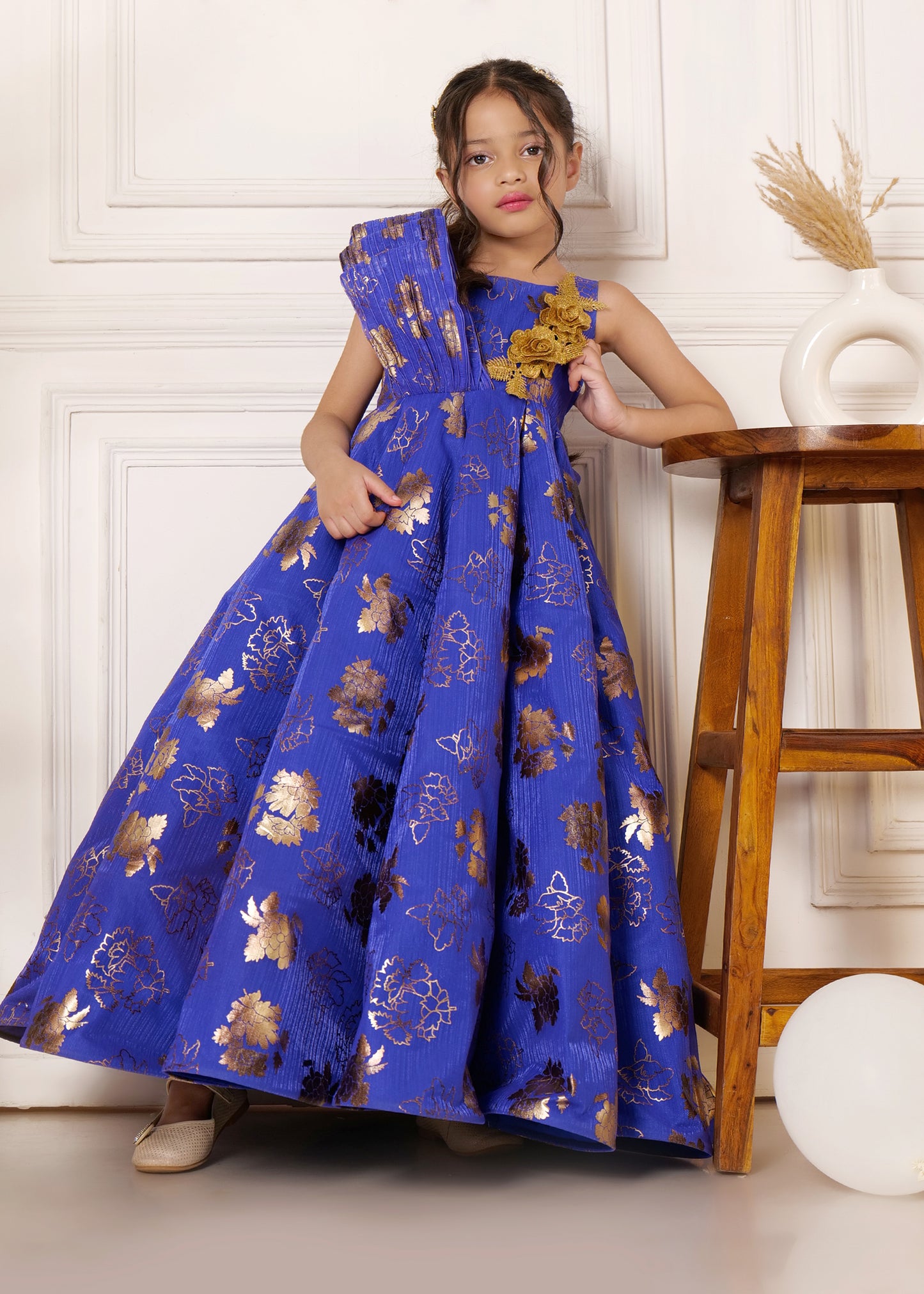 Girl wearing a royal blue floral dress with golden detailing, showcasing elegant design with a flower accessory on the shoulder