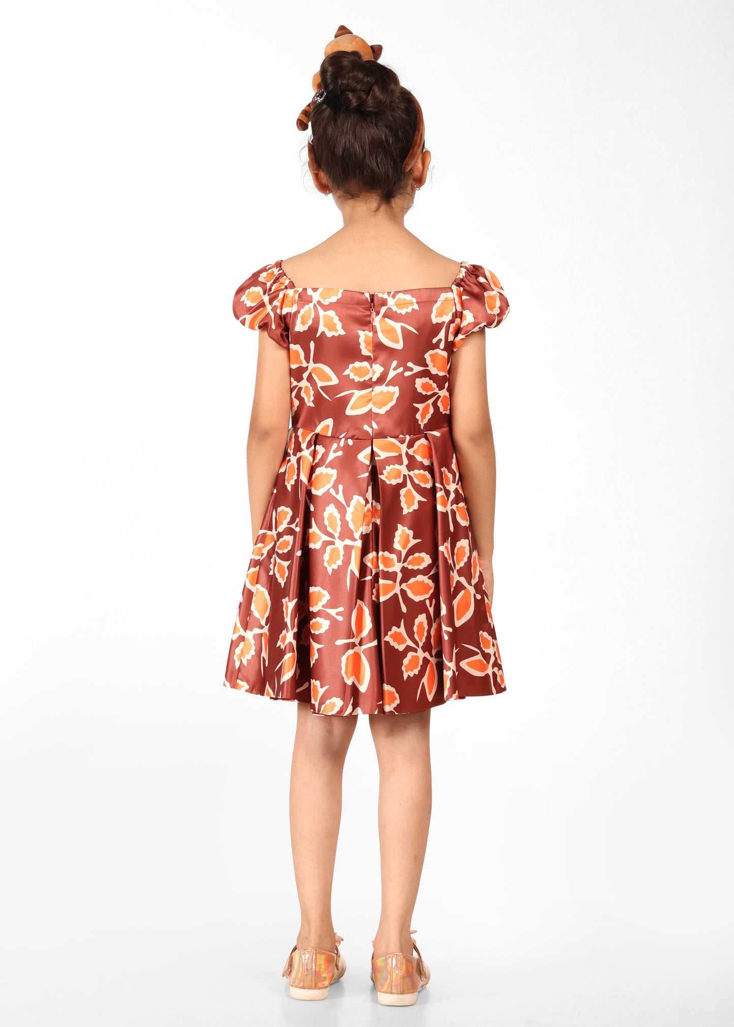 Back view of a young girl in a brown floral dress with puffed sleeves, showcasing the elegant pleated skirt design