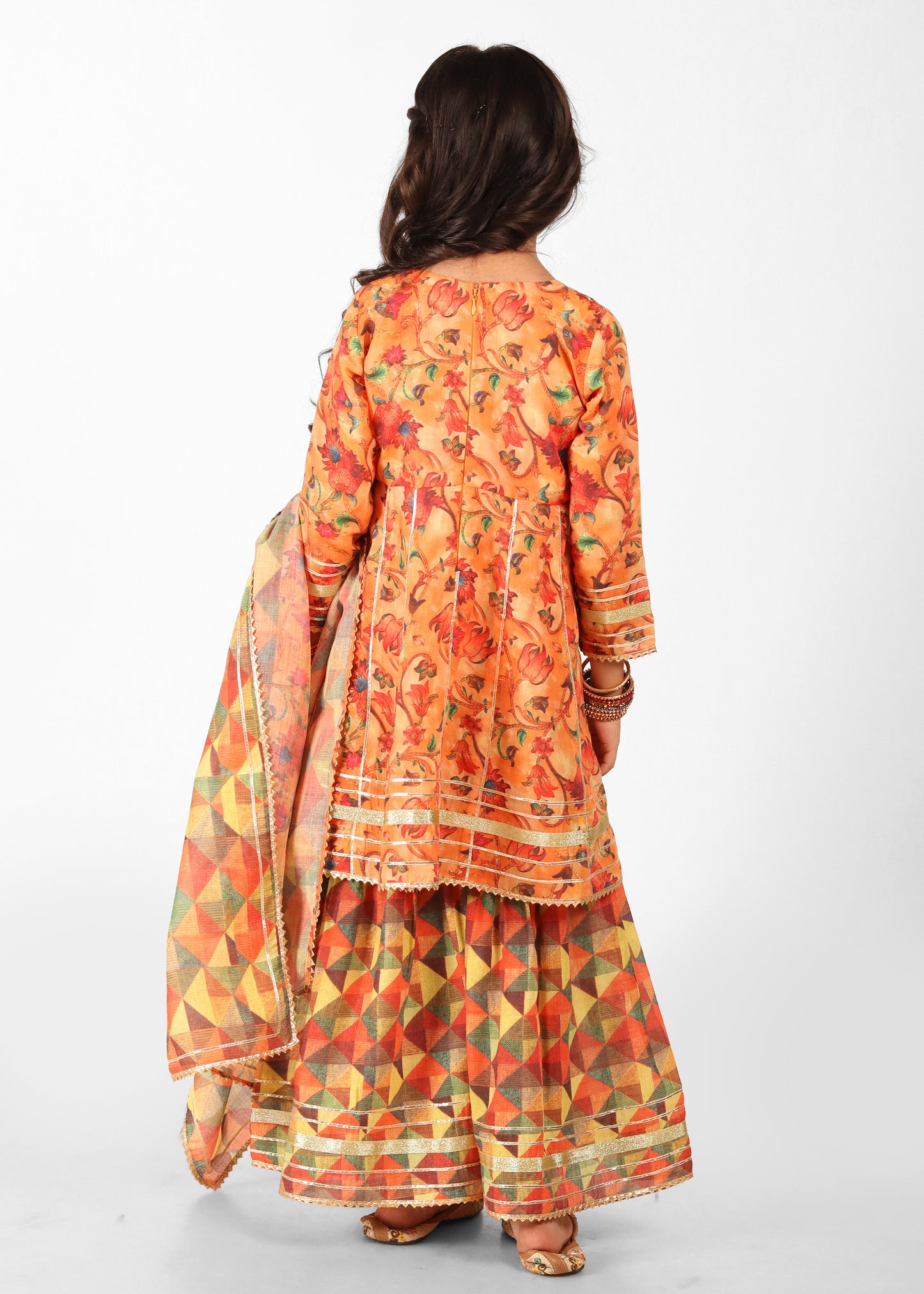 Rear view of a young girl showcasing her festive orange floral kurta paired with a geometric palazzo and dupatta. The ethnic outfit is highlighted by beautiful patterns and detailing, ideal for festive occasions.