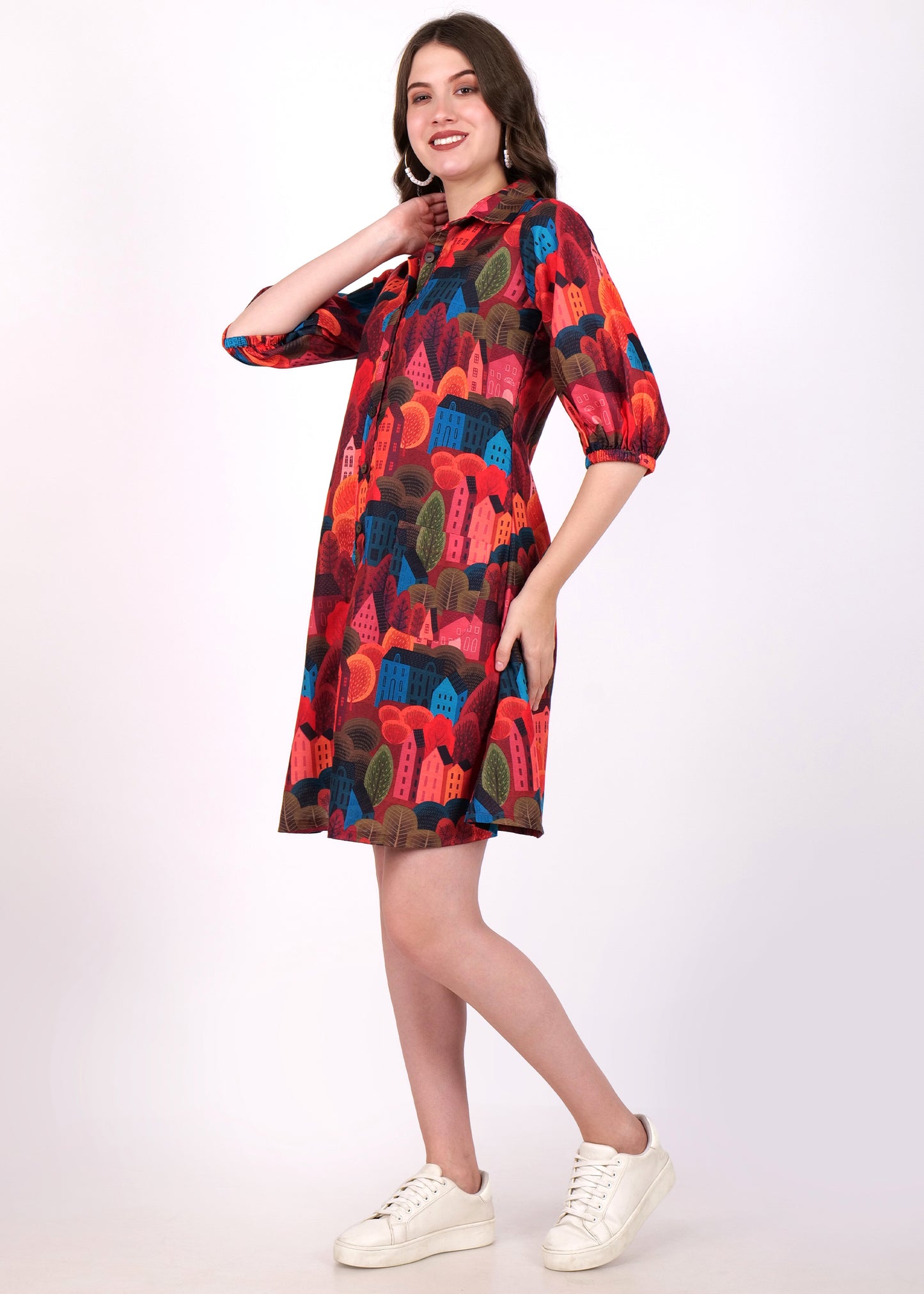 "Side view of a model in a colorful abstract house print shirt dress with vibrant red and blue tones, paired with casual white sneakers."