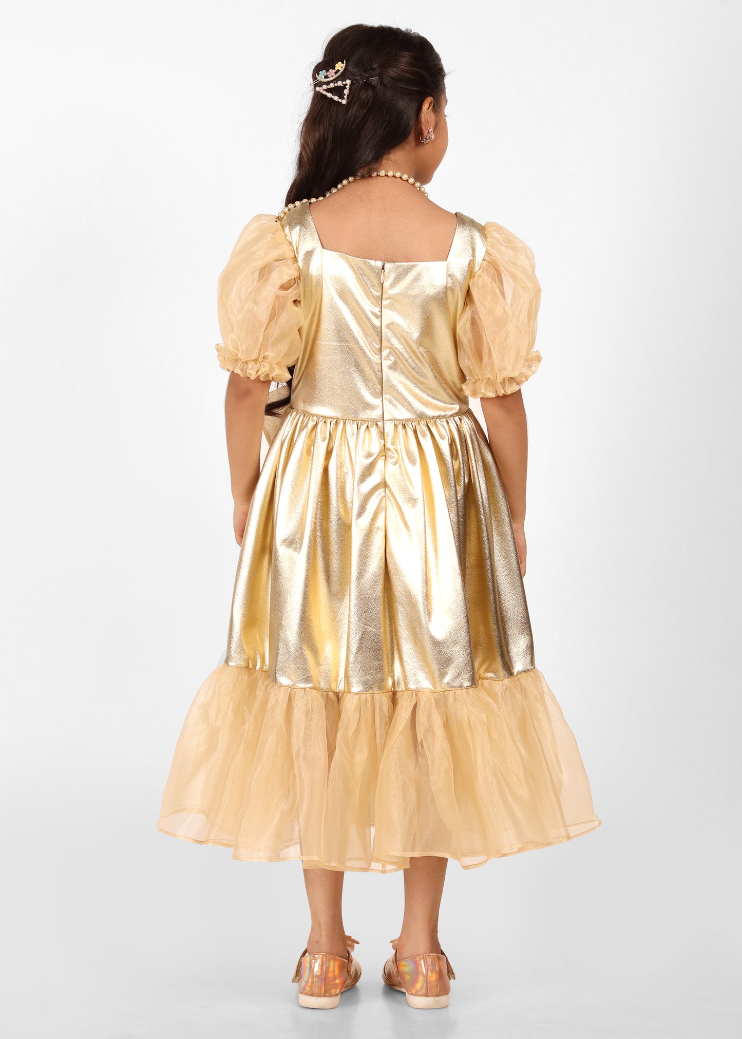A back view of a girl in a gold puff-sleeved gown, showing the flowing silhouette and elegant design, complemented by a festive hairstyle.