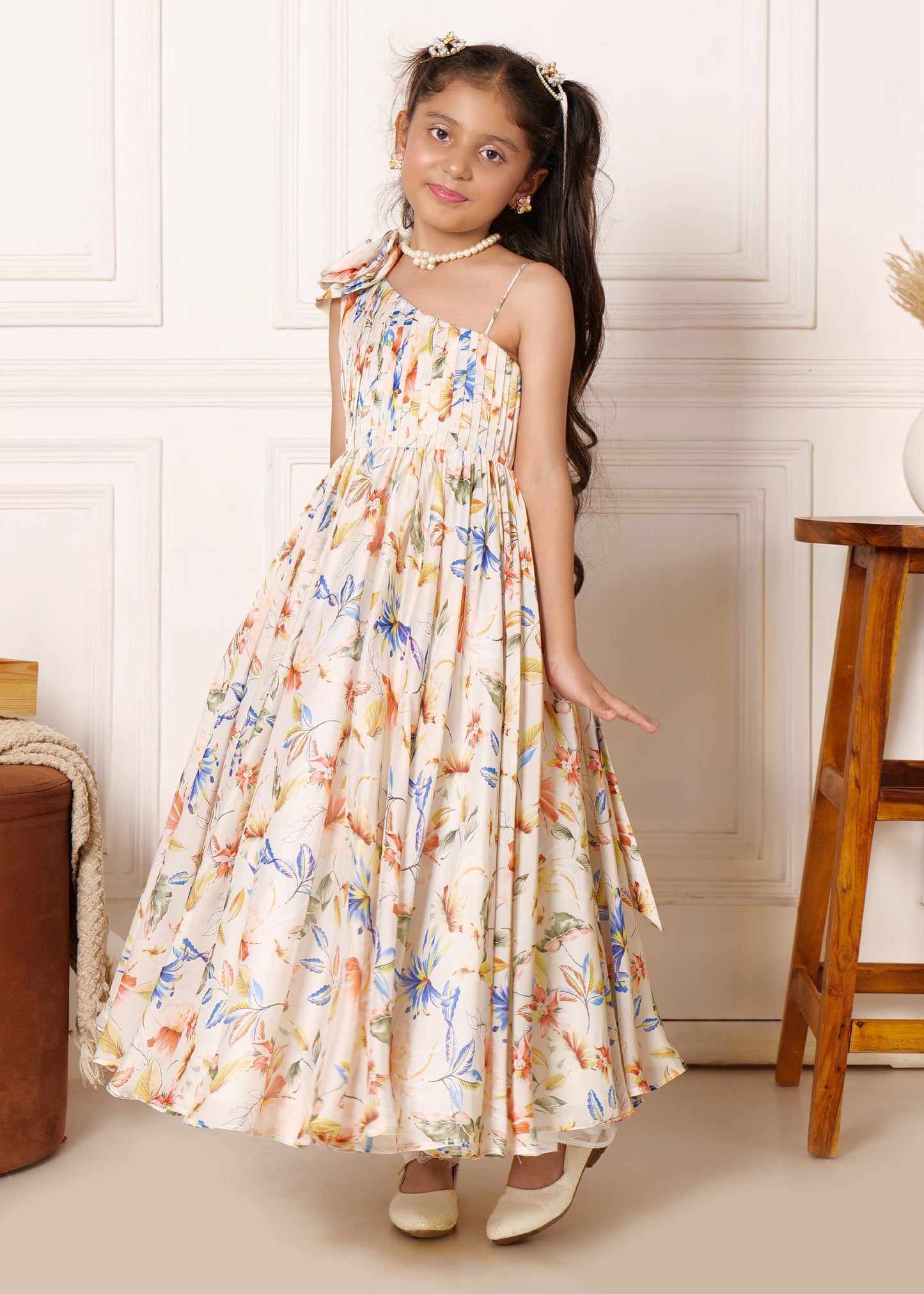 Young girl in a vibrant floral print gown, gracefully posing with a one-shoulder design and natural flowy fabric