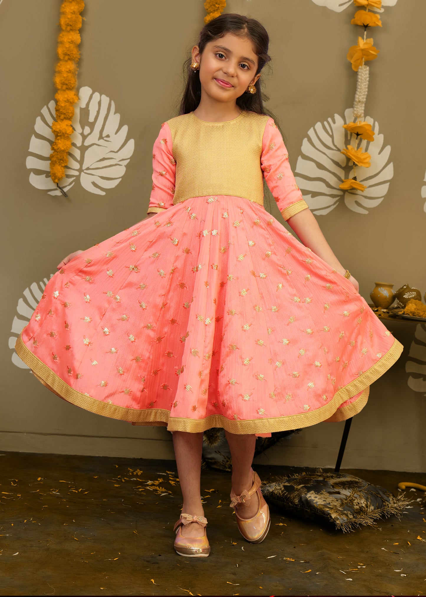 Smiling girl twirling in a peach and gold ethnic dress, showcasing intricate embroidery and festive charm.