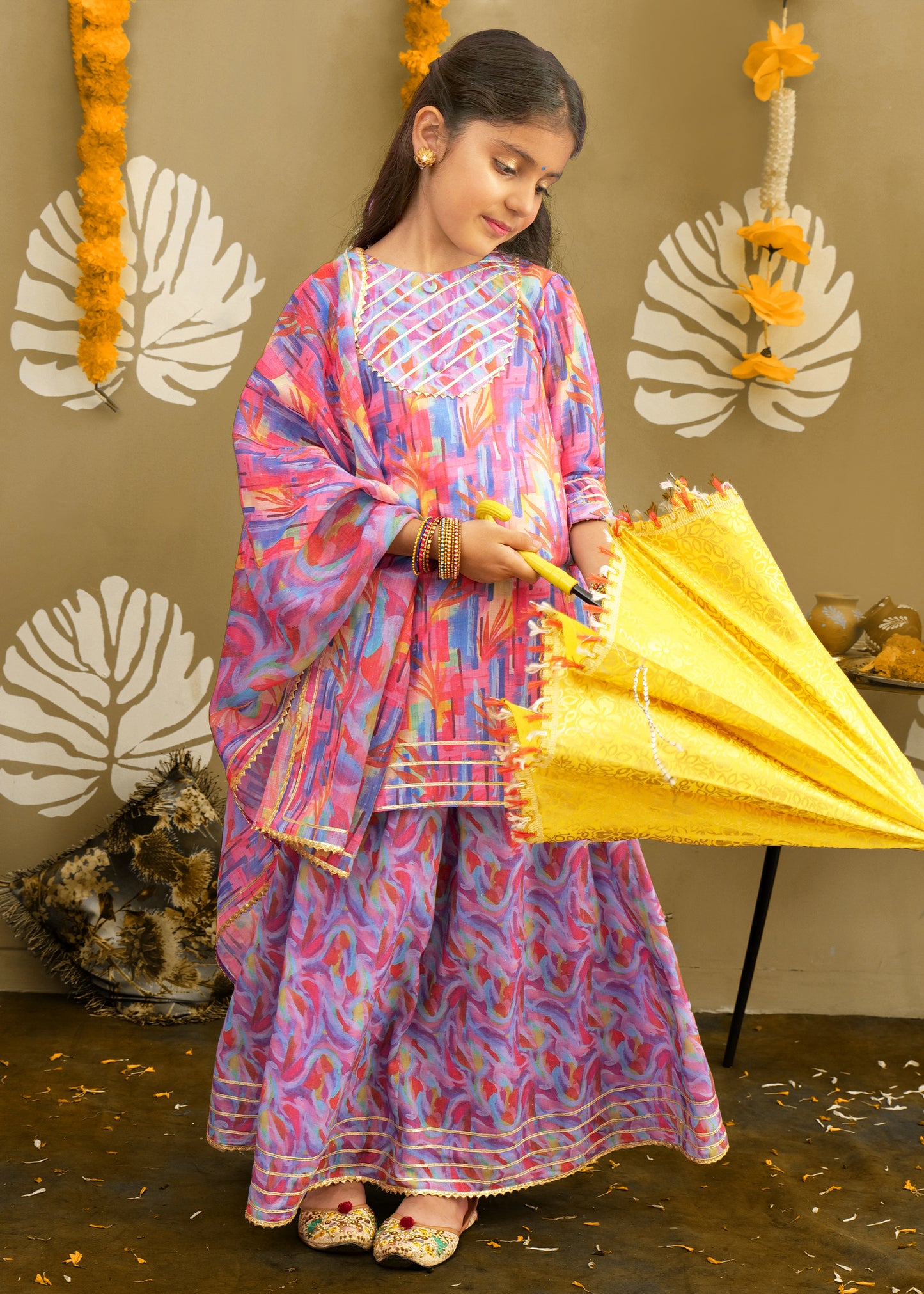 The same girl gracefully holding a decorative yellow umbrella, wearing a colorful traditional ensemble with intricate embroidery, perfect for festive celebrations.