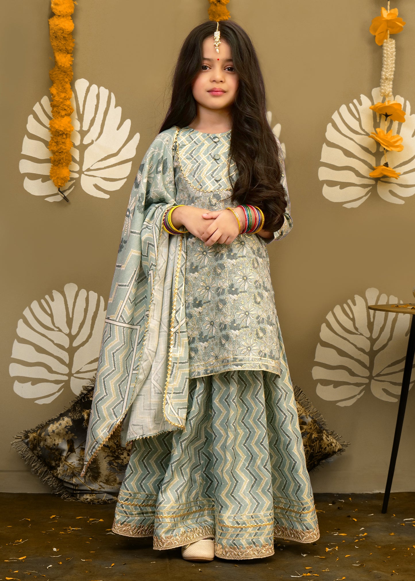 "Young girl in a pastel green ethnic wear featuring intricate floral embroidery and chevron pattern, posing for a photoshoot."