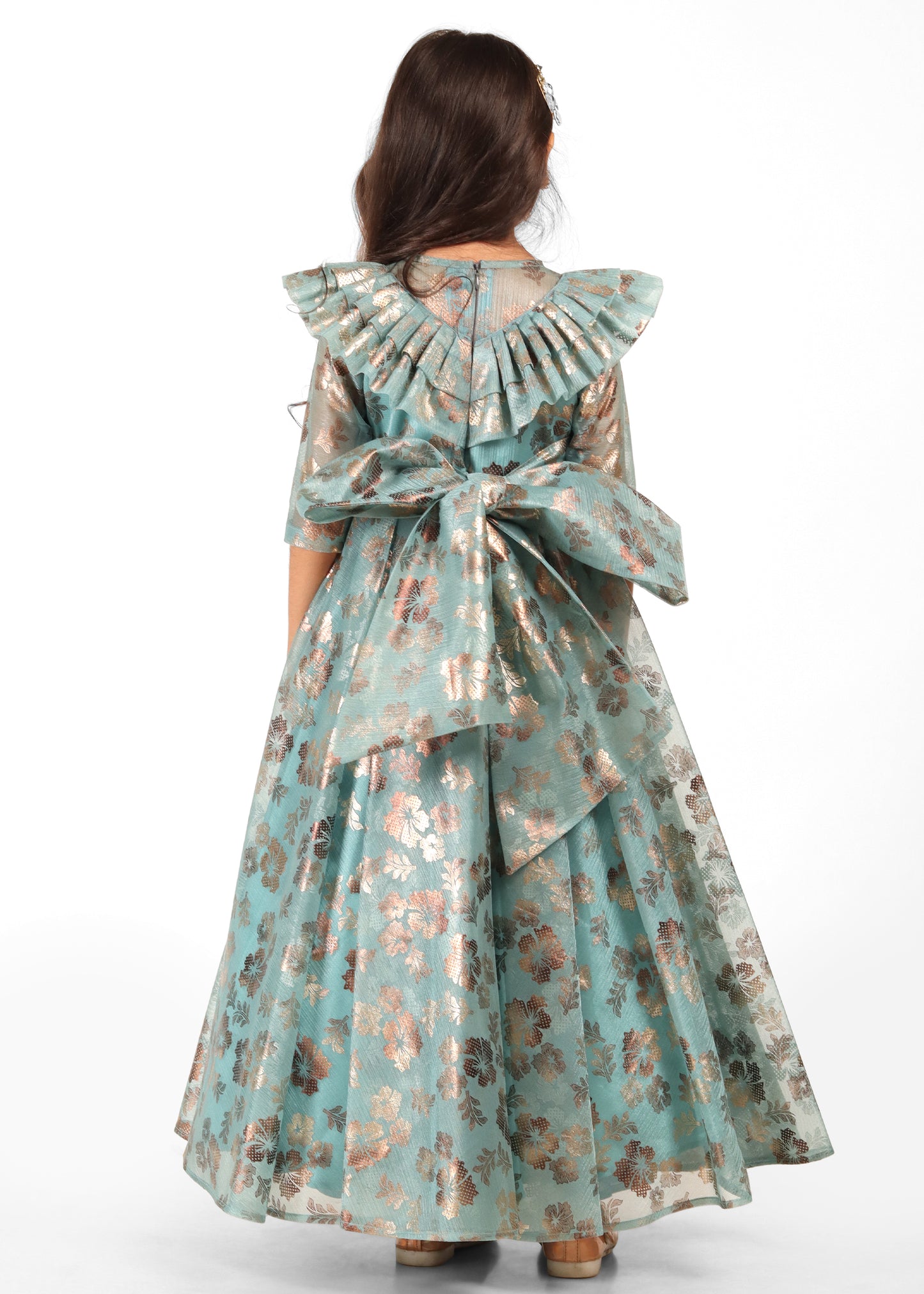 Back view of a teal floral gown featuring a large decorative bow, worn by a girl with long hair and festive hair accessories.