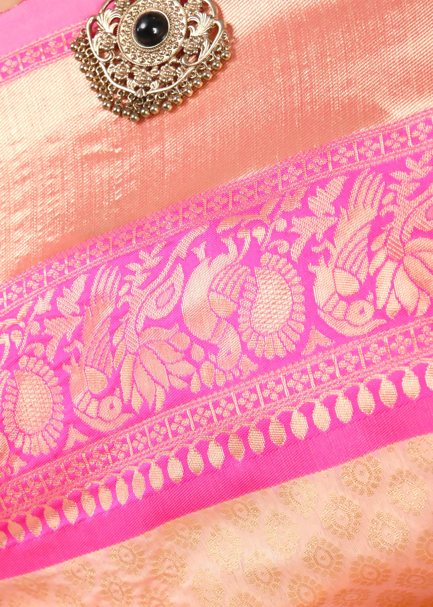 Close-up of the luxurious zari work on the border of the peach and pink saree, featuring floral and peacock motifs