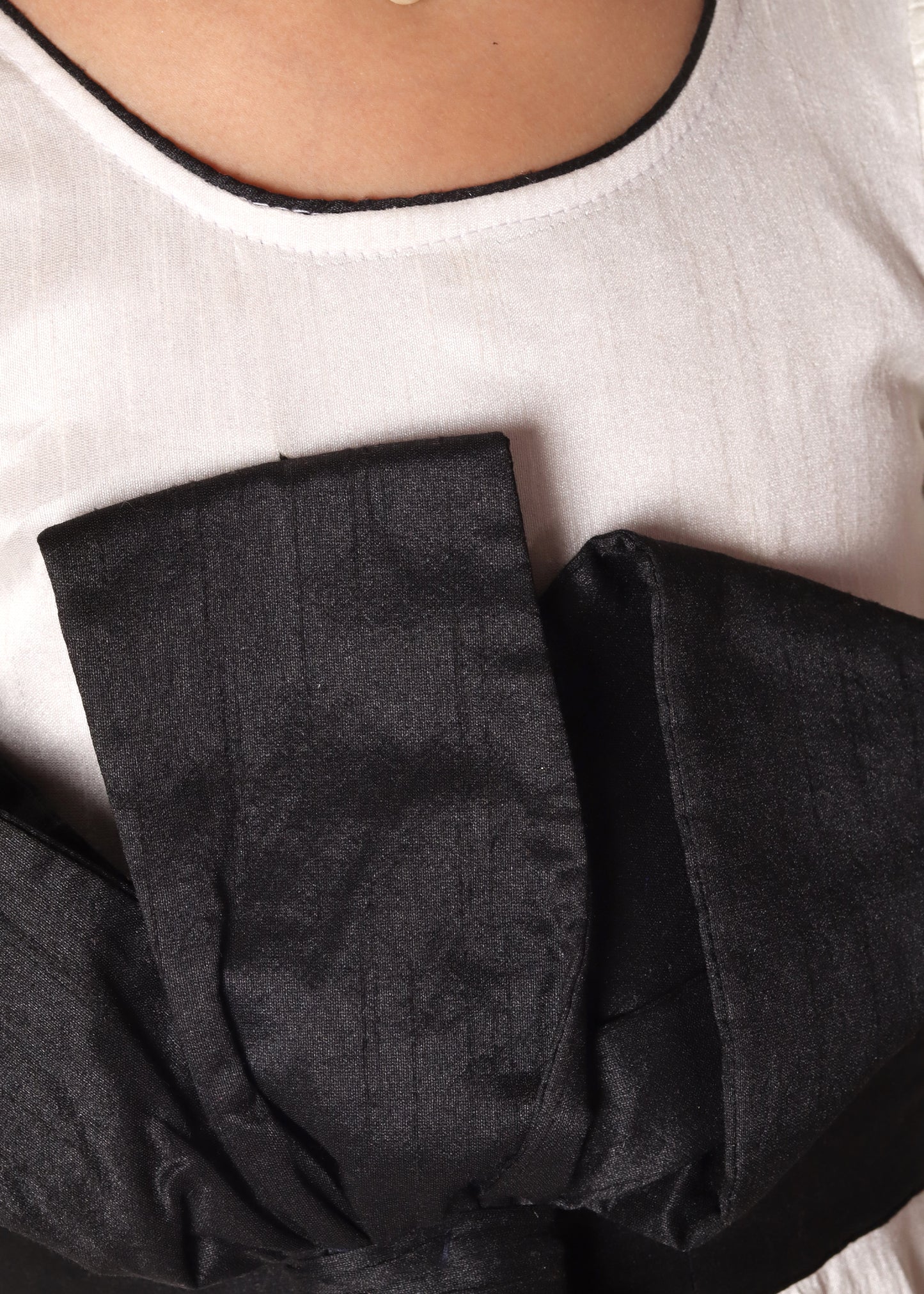 Close-up of a large black bow detail on a white girl's dress, highlighting the elegant design and contrasting colors