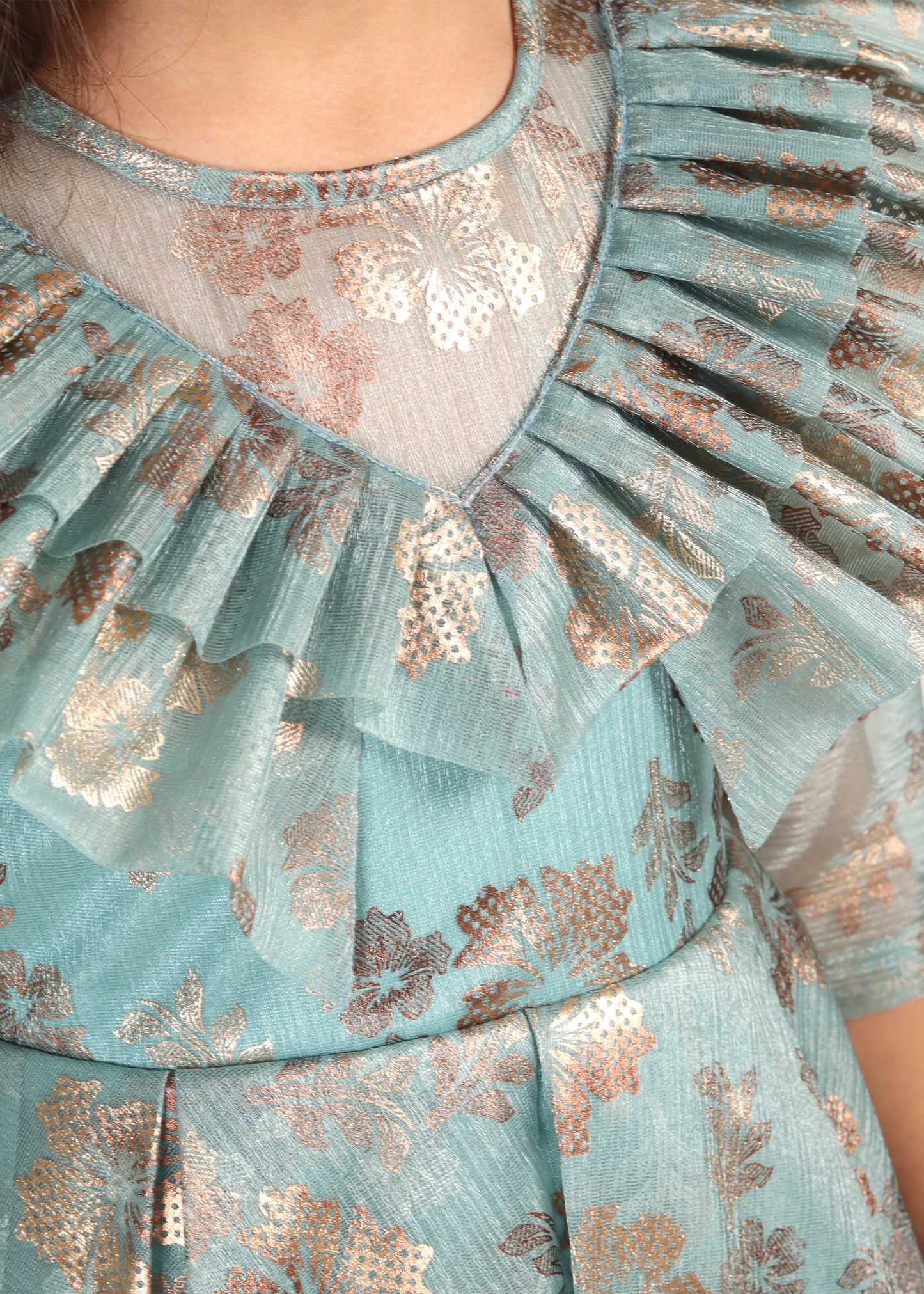Close-up of the ruffled collar and floral gold accents on a teal gown, highlighting the intricate detailing of the dress fabric.