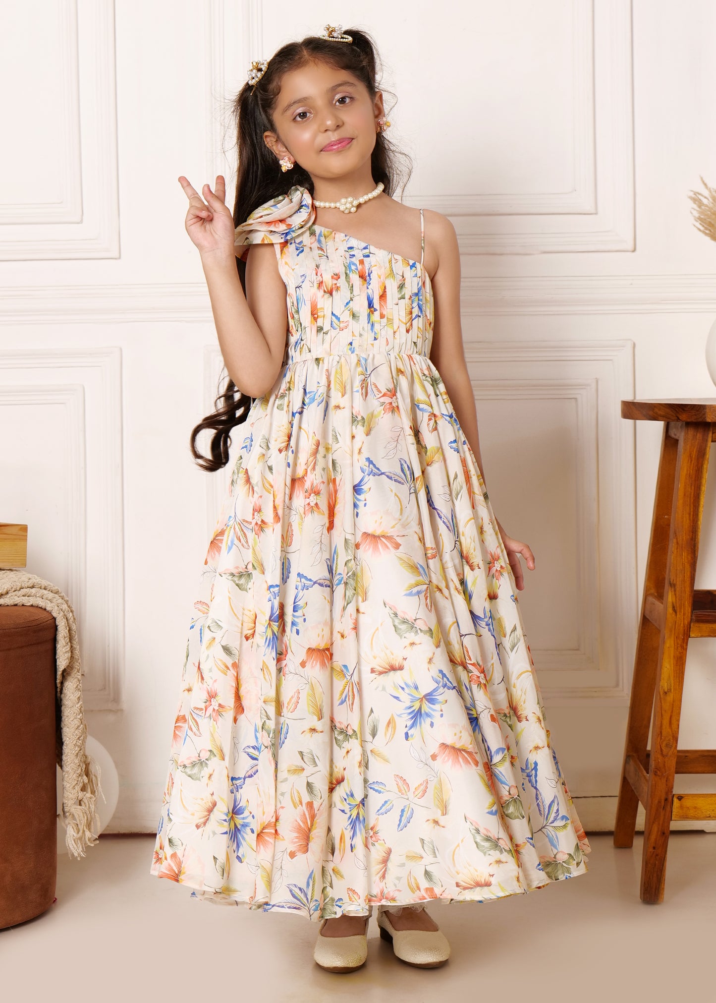 Smiling girl wearing a floral maxi dress with a pleated bodice, showcasing a peaceful pose with a one-shoulder floral detail