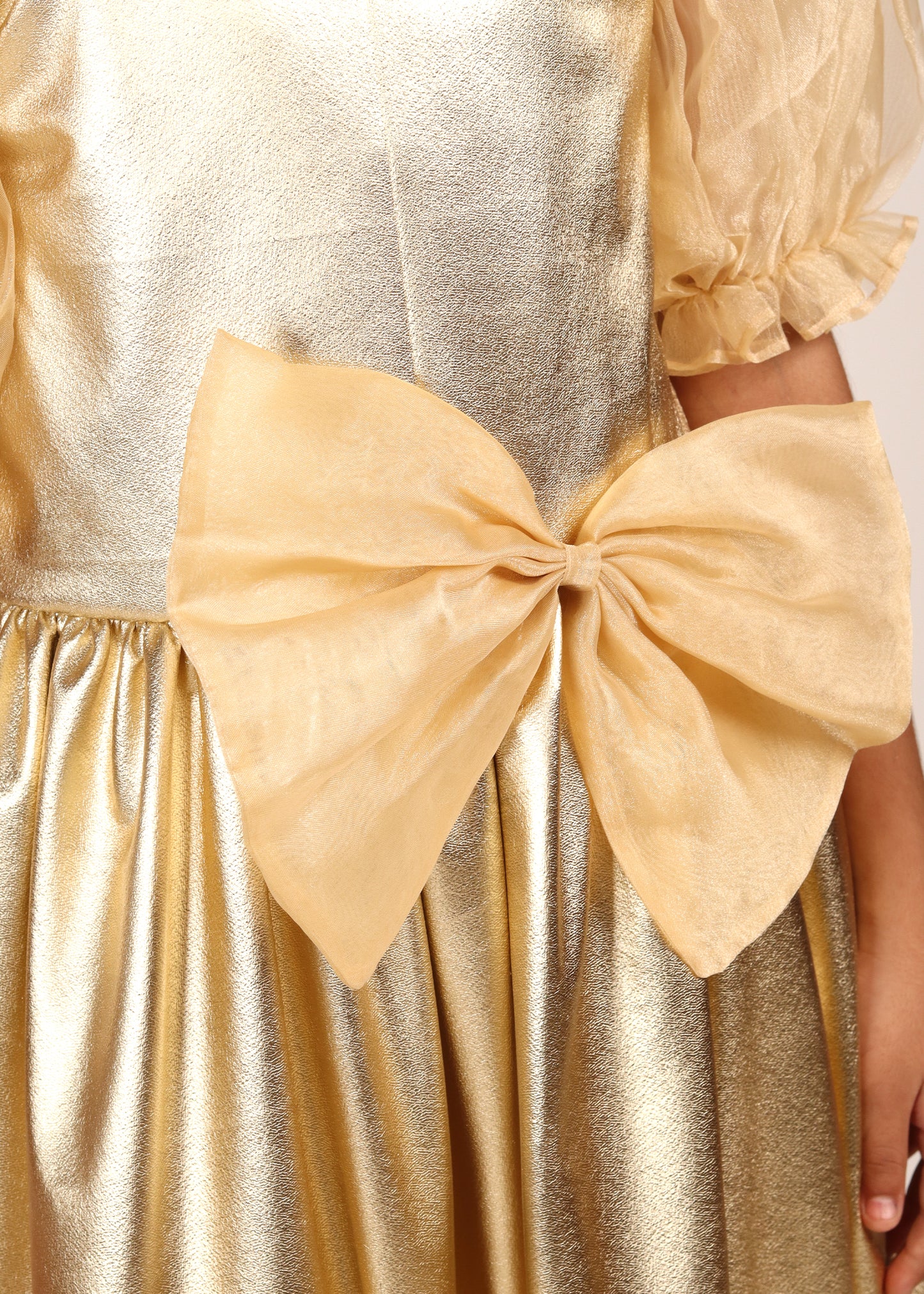 Close-up of a large golden bow detail on a shimmering dress, highlighting the luxurious fabric and intricate design of the outfit.