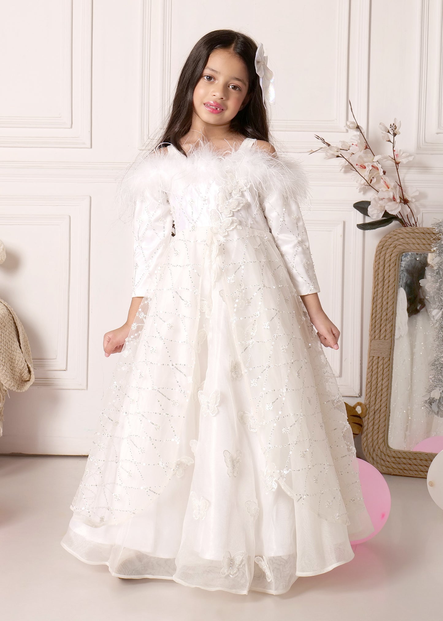 Girl posing in a white fairy-like dress adorned with delicate butterflies and sparkly sequin designs, showcasing her angelic gown.