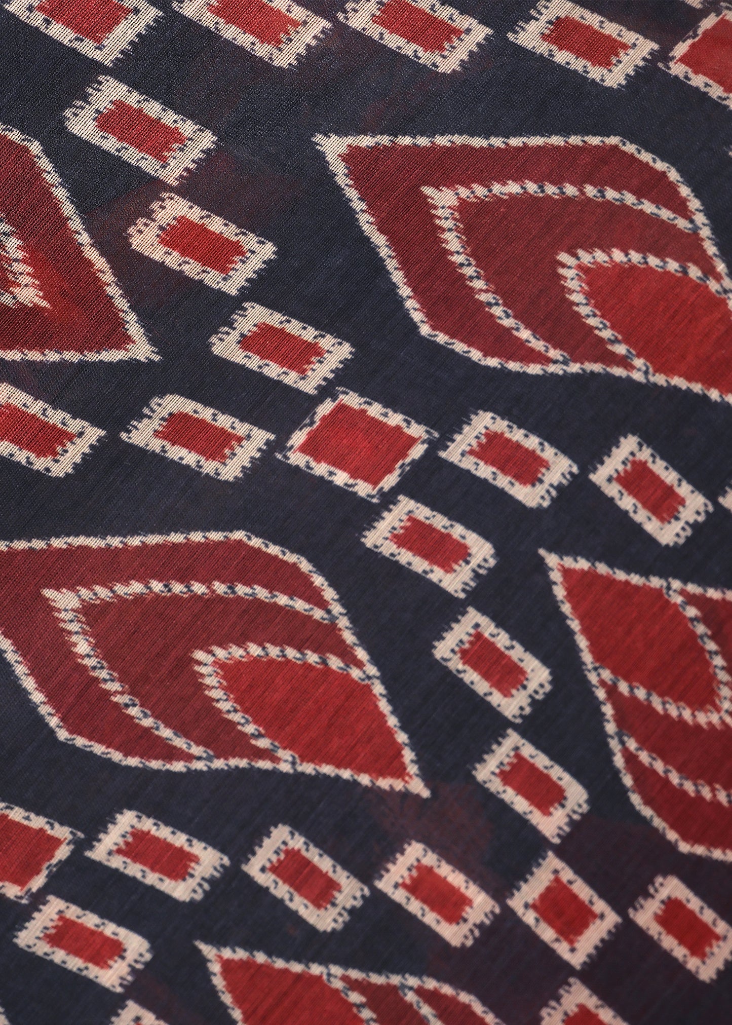Close-up of the red and black saree's intricate geometric pattern, highlighting the detailed craftsmanship on the fabric.