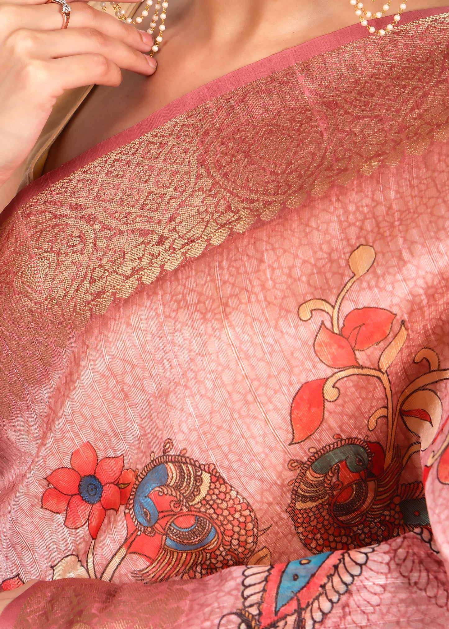 Close-up of a luxurious pink silk saree featuring golden borders and colorful peacock motifs, highlighting the detailed craftsmanship