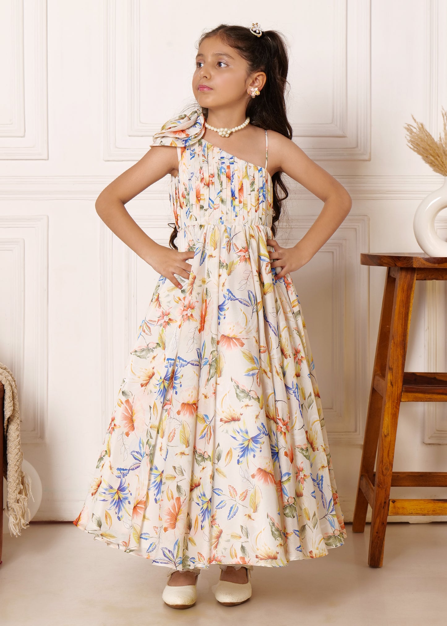 Charming girl in a full-length floral gown, striking a confident pose with a floral pattern and elegant pleats