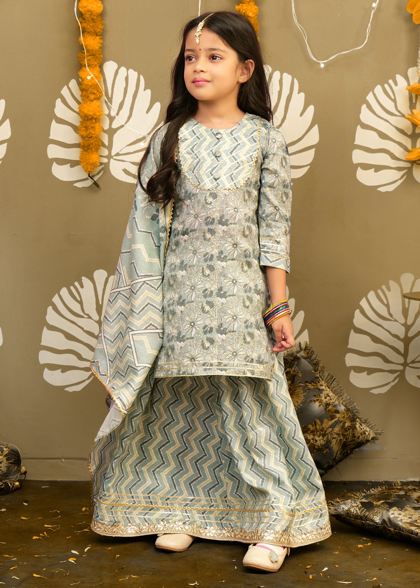 "Close-up of a girl's pastel green outfit with detailed floral embroidery and delicate gold accents."
