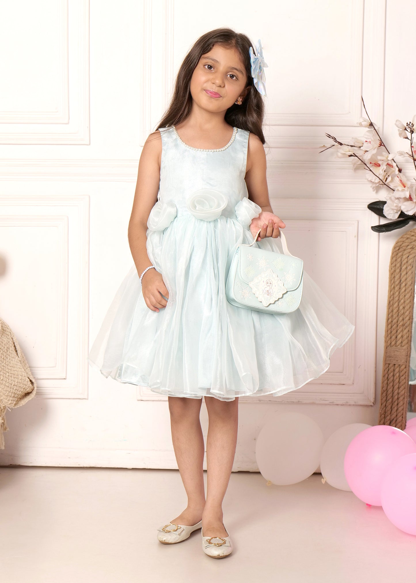 The girl playfully twirls in a lovely pastel blue floral dress, accentuated by soft fabric flowers and matching blue hair accessories.