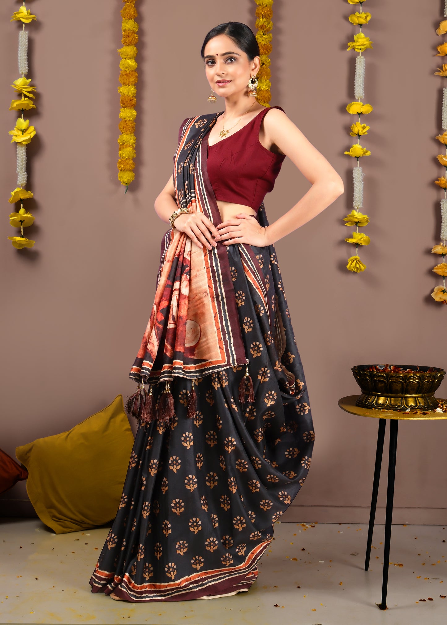 Traditional Indian black saree with intricate floral motifs, styled with a maroon sleeveless blouse and gold earrings