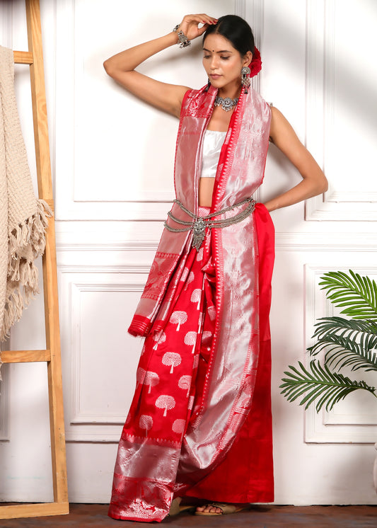 Model gracefully leaning against a wall in a red saree with silver motifs, styled with a statement belt for a unique bridal look