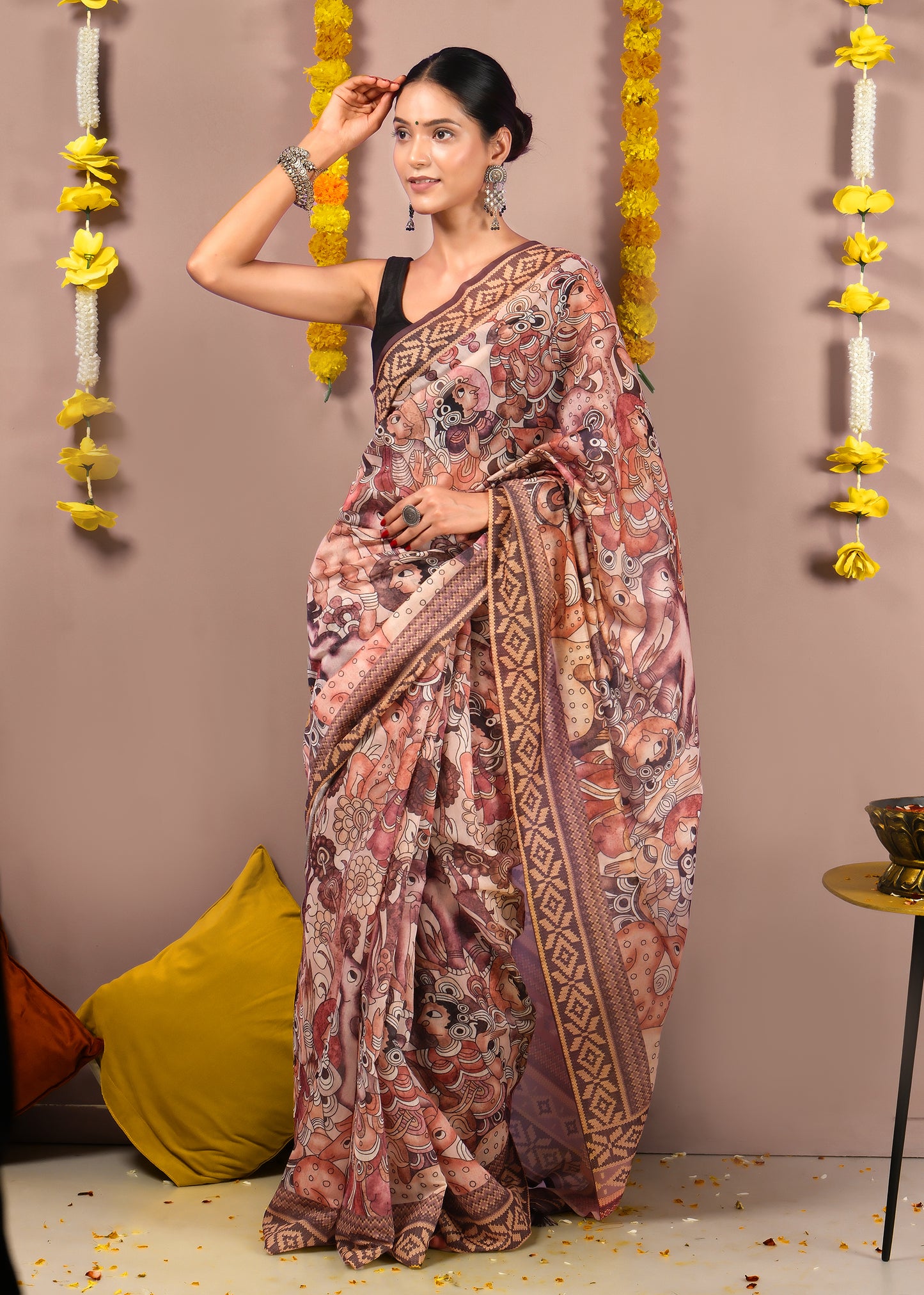"Full view of a saree with mythological motifs, woman standing elegantly against a floral decor background."