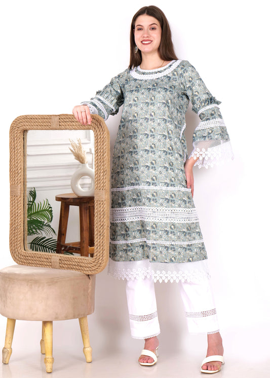 Woman leaning on a mirror, dressed in a floral green kurta with lace embellishments, paired with white pants and heels