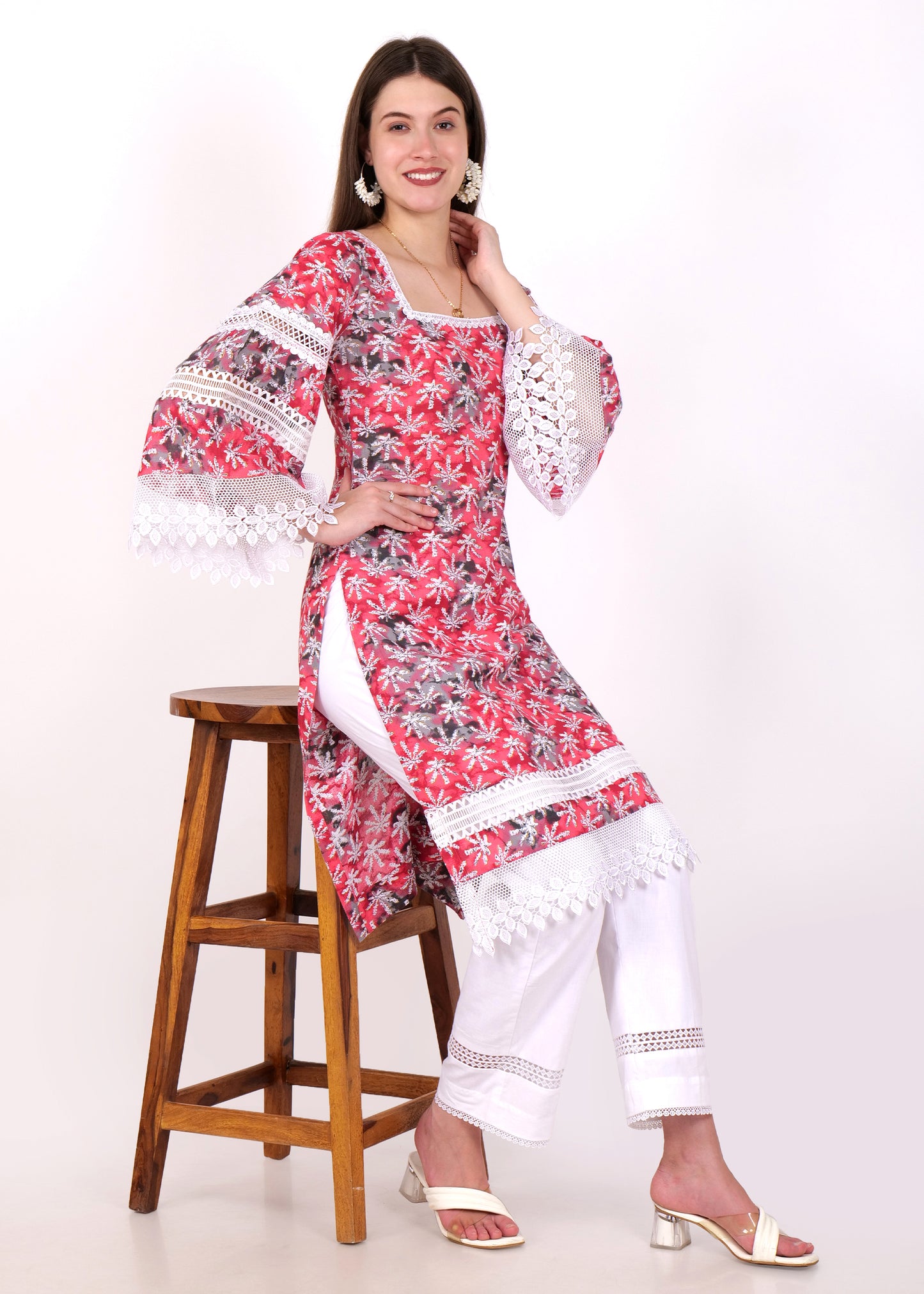 "Model sitting in a red floral printed kurti with white lace detailing on sleeves, paired with white pants"