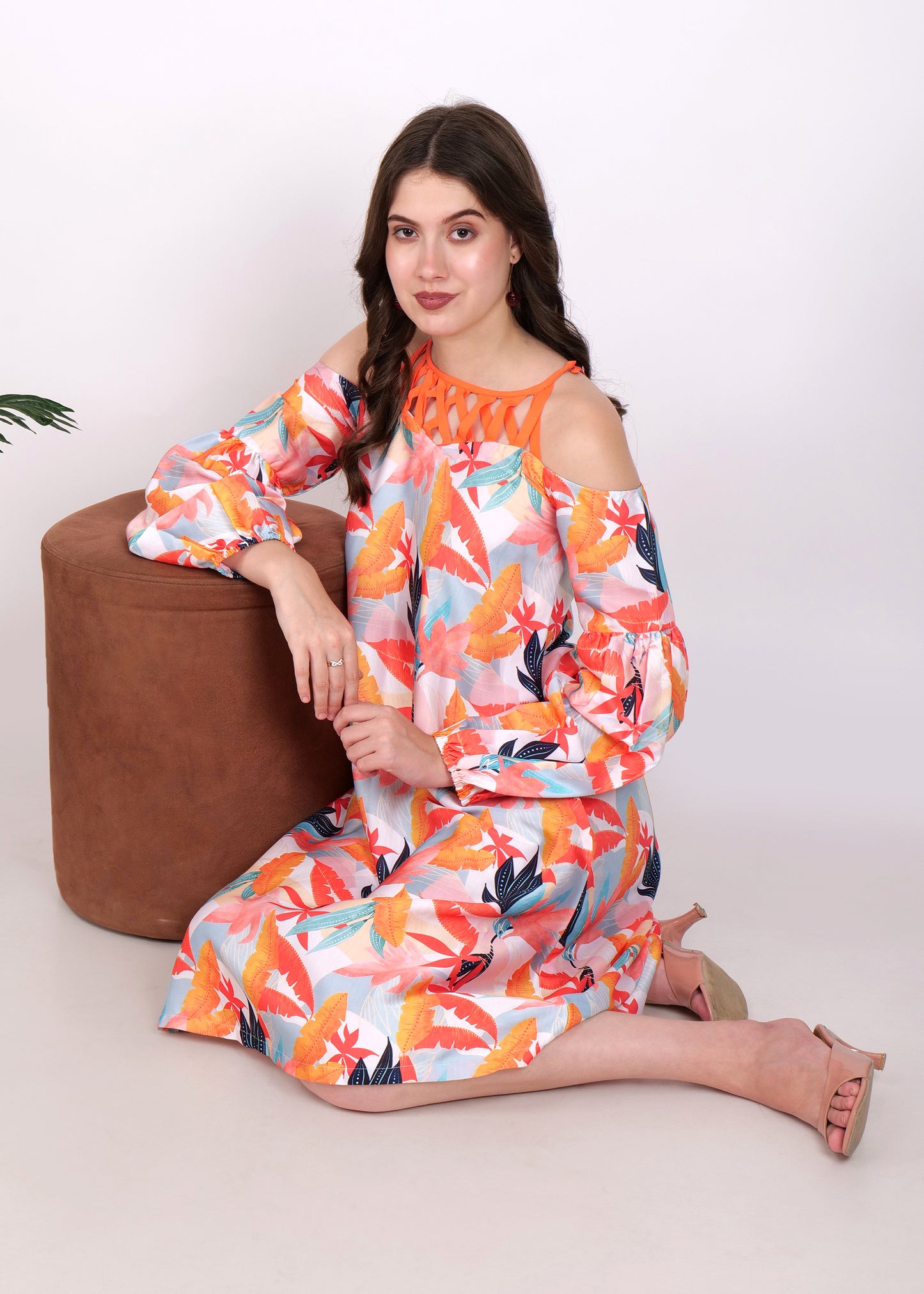 Model sitting with a relaxed pose in a colorful off-shoulder tropical leaf print dress with balloon sleeves.