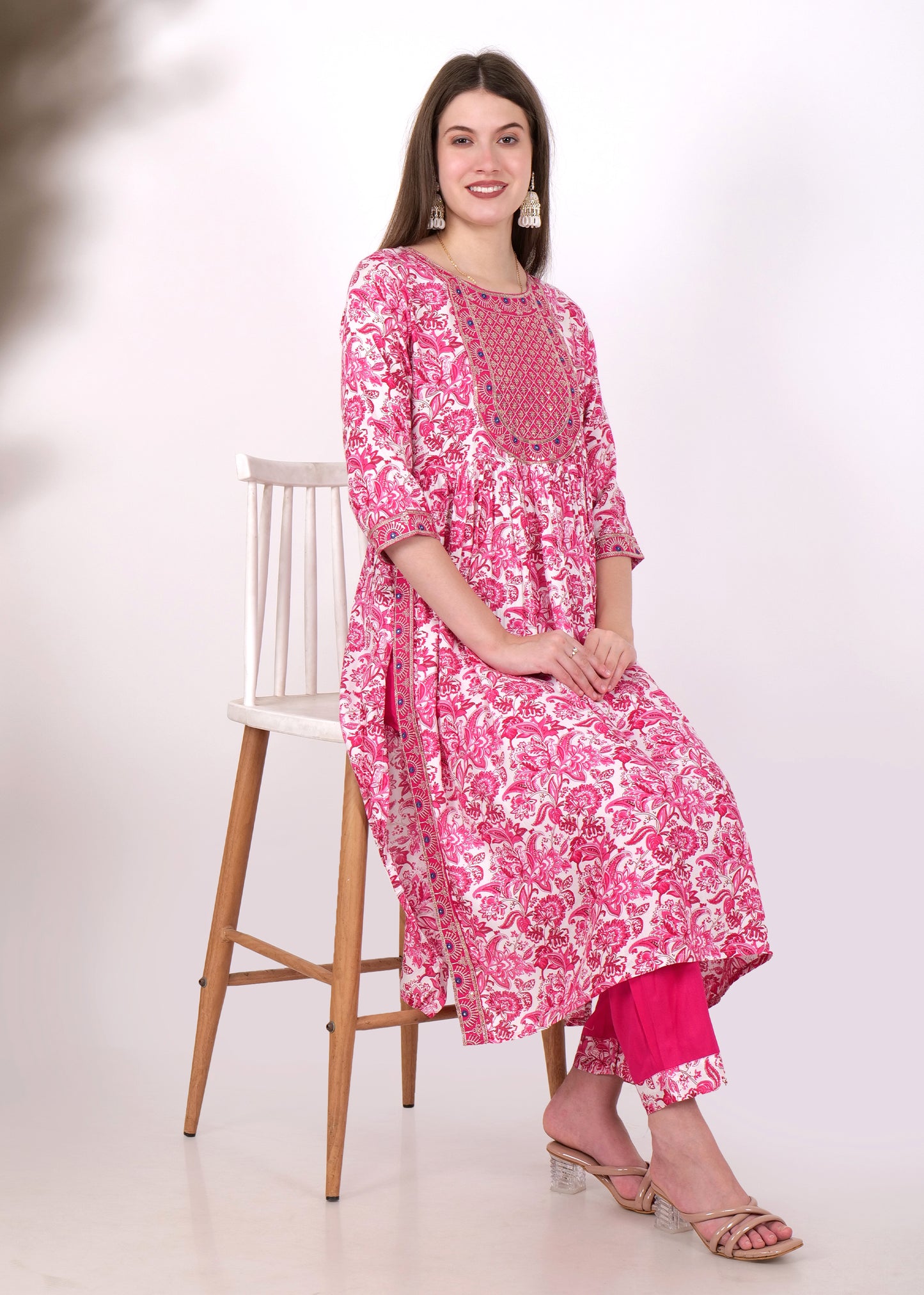 Woman elegantly seated, wearing a pink embroidered kurta set, looking fashionable and graceful.
