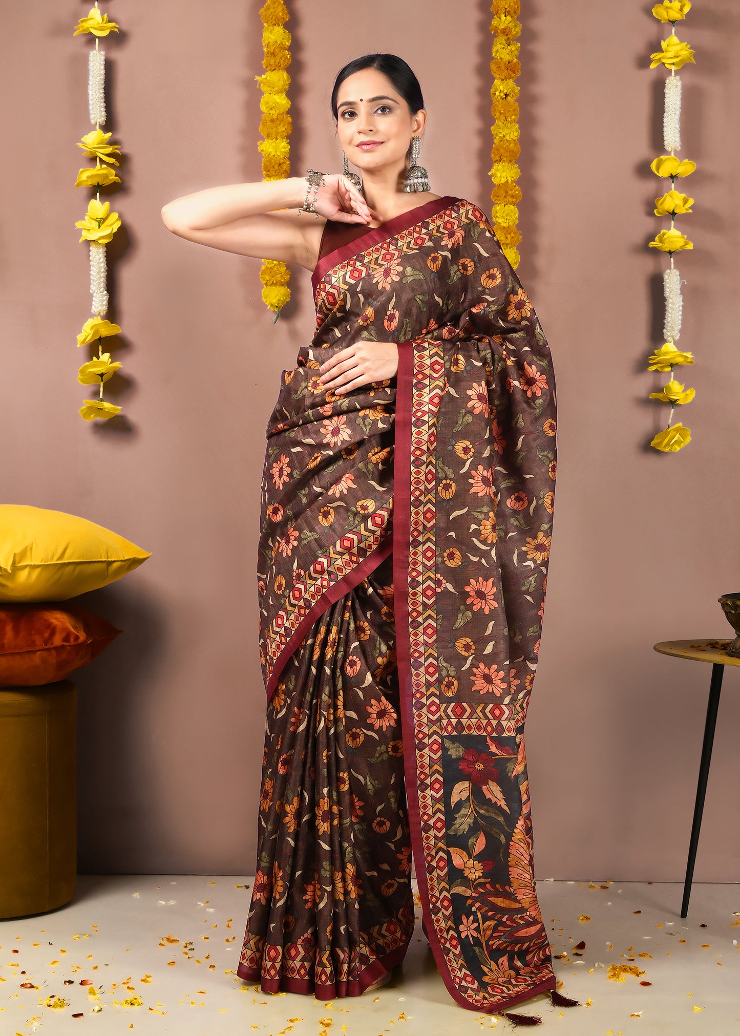 Woman elegantly posing in a brown floral printed saree with a bold red border, styled for a traditional Indian celebration.