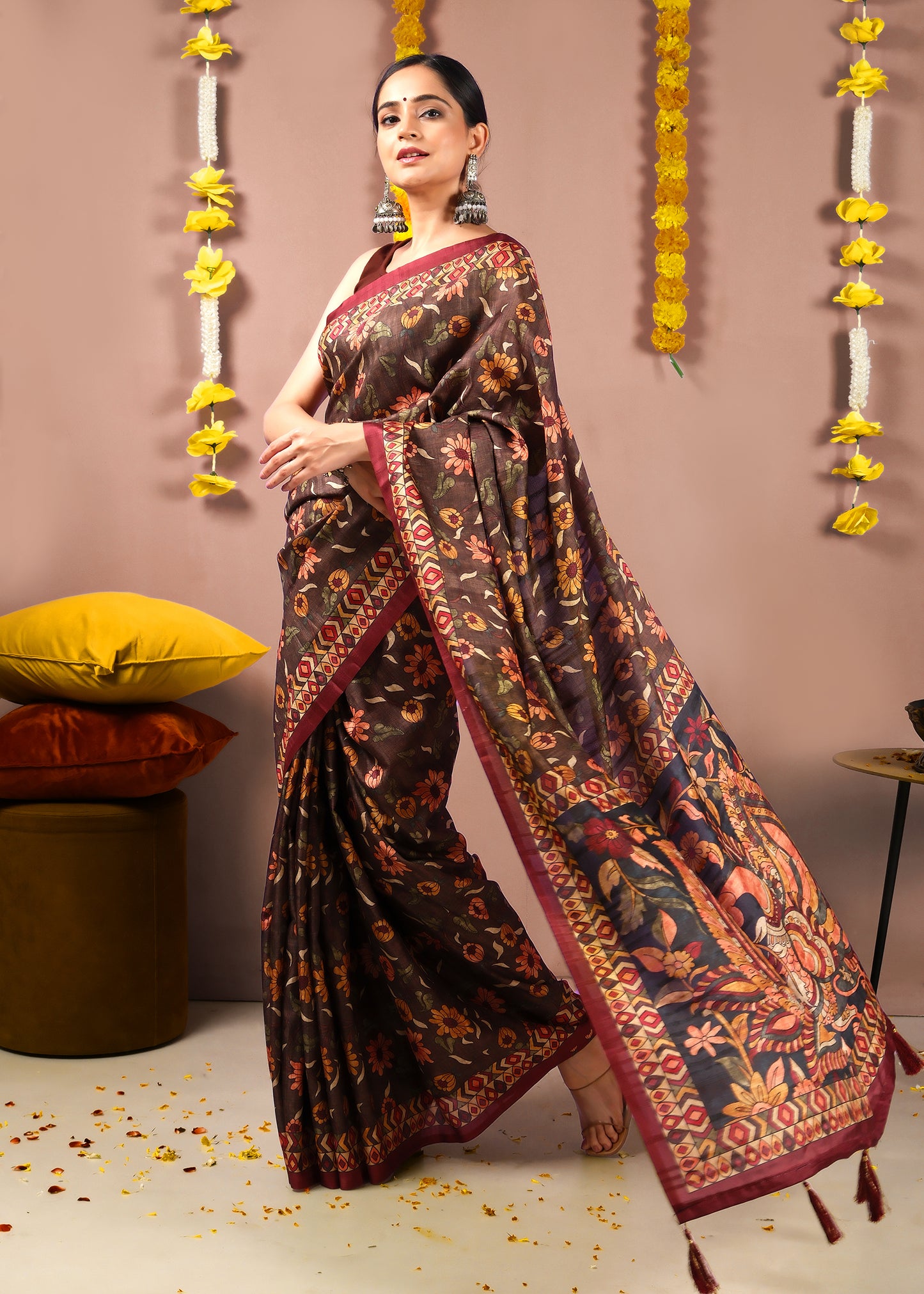 ull view of a woman wearing a rich brown saree with intricate floral embroidery and peacock motif on the pallu, styled for an Indian festival.