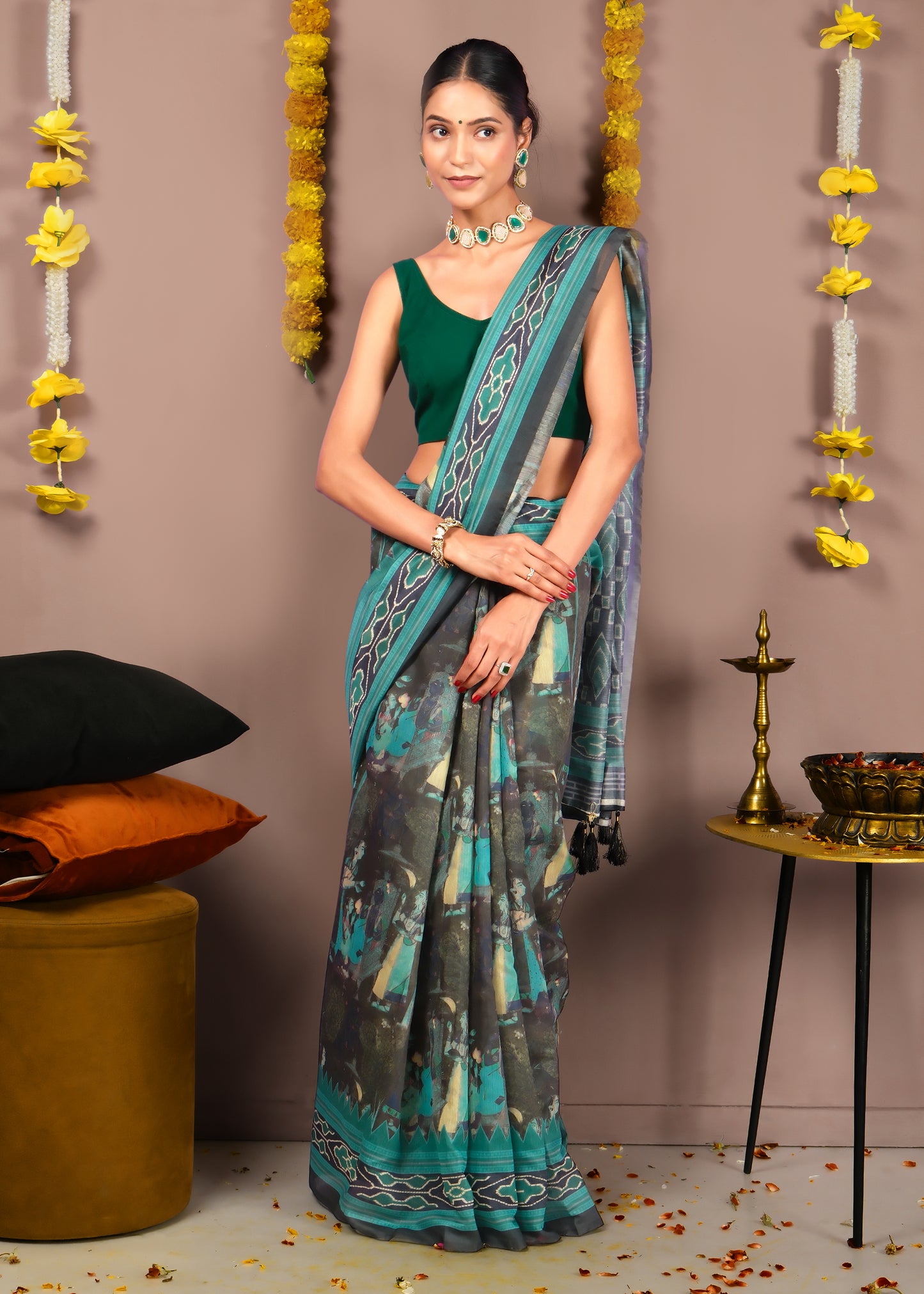 Model wearing a green and black saree with intricate designs, accessorized with a choker necklace and traditional decor in the background