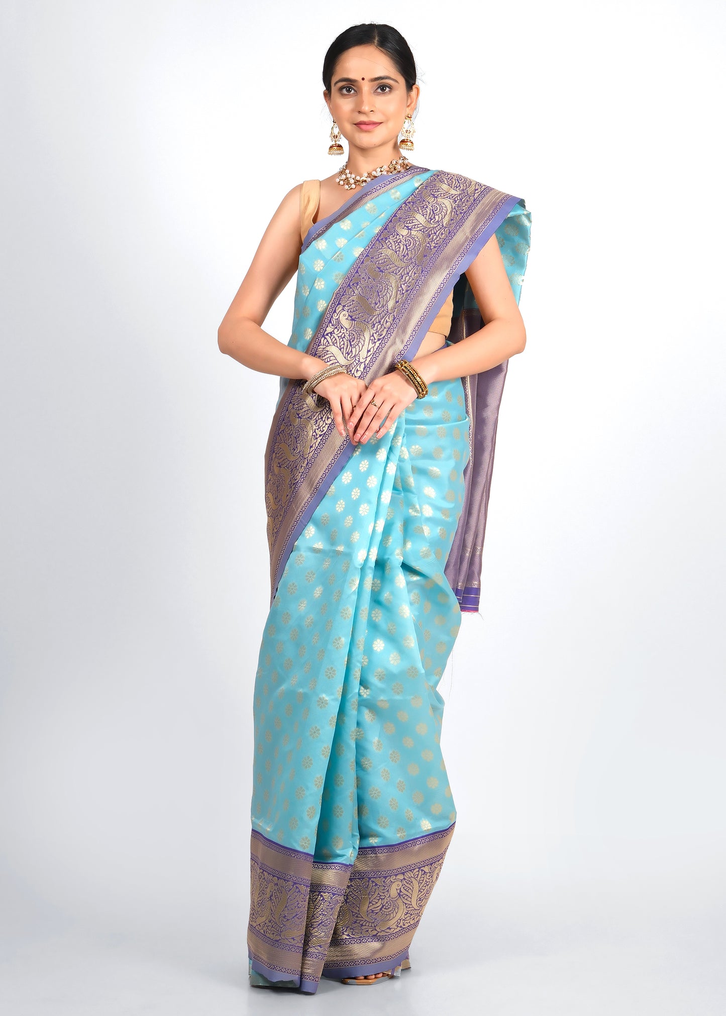 Woman draped in a traditional turquoise blue silk saree with intricate purple and gold zari border, showcasing timeless Indian ethnic wear.