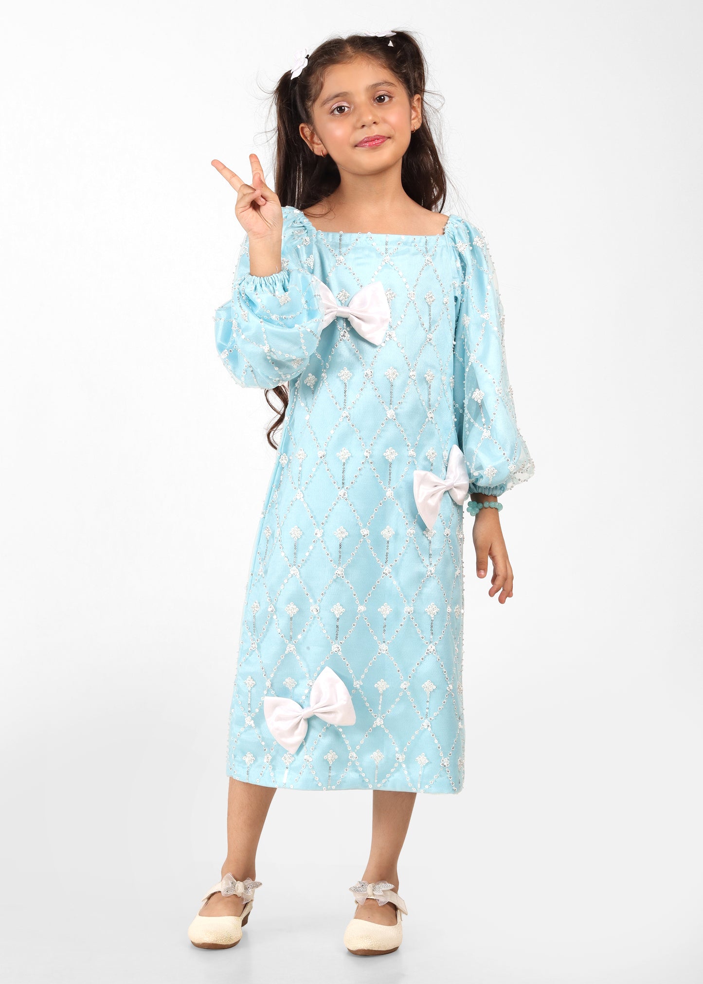 Little girl in a light blue embroidered dress adorned with white bows, sitting on a stool while reading a book, showcasing her stylish and elegant outfit.

