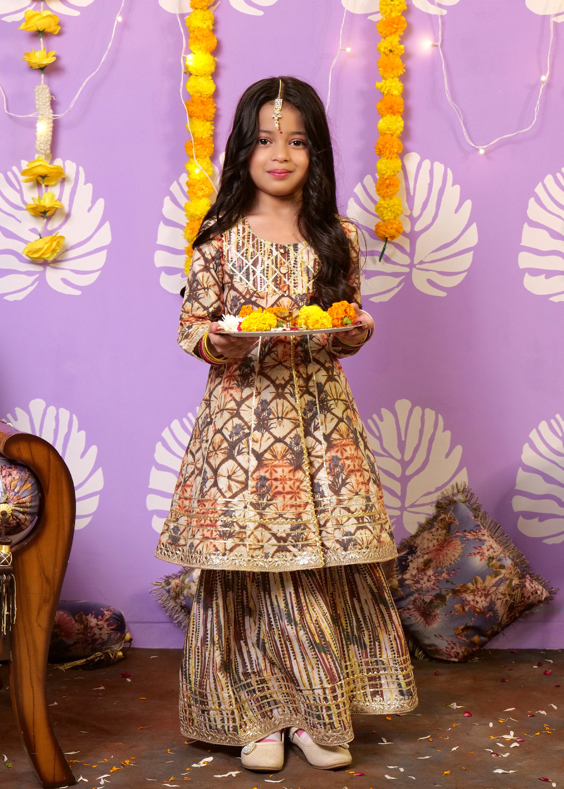 Young girl in an intricate traditional Indian ethnic outfit, holding a vibrant plate of marigold flowers, celebrating a festive occasion.