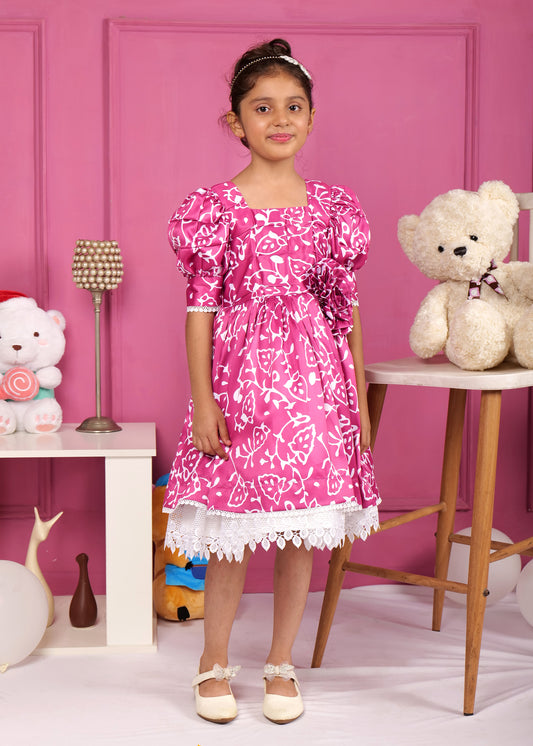 Little girl wearing a vibrant pink puff sleeve dress with floral patterns, standing confidently in front of a pink backdrop with soft toys