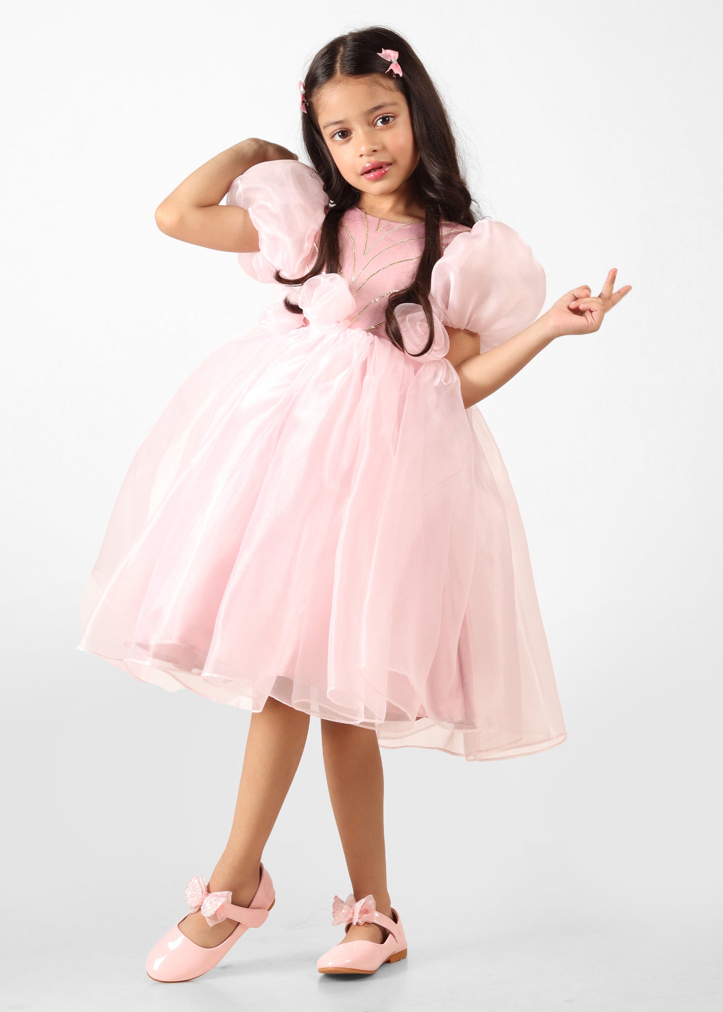 "Full view of a girl in a pink puff-sleeve organza dress, displaying the flared skirt and floral details, showcasing the perfect party look."