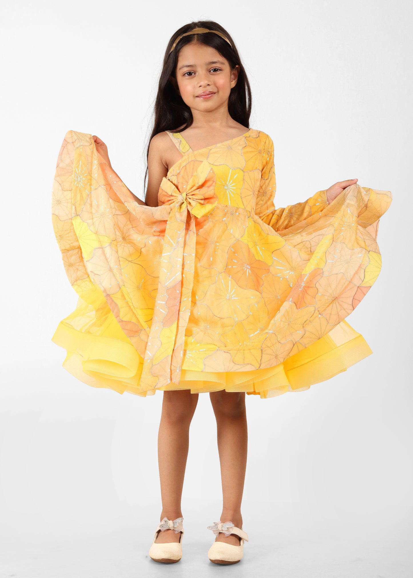 "Adorable girl wearing a yellow floral print one-shoulder dress with a bow, ideal for special occasions or festive events."