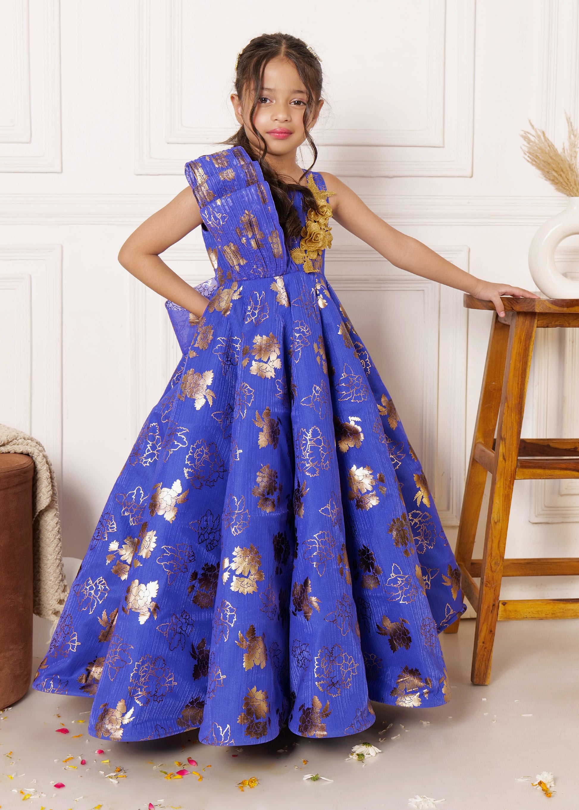 Girl in a royal blue gown with golden floral patterns, posing confidently next to a stool, perfect for festive occasions