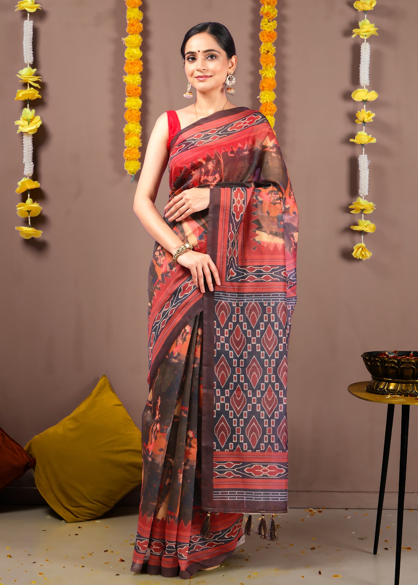 Woman in a traditional red and brown Ikat saree with bold geometric patterns, standing gracefully.