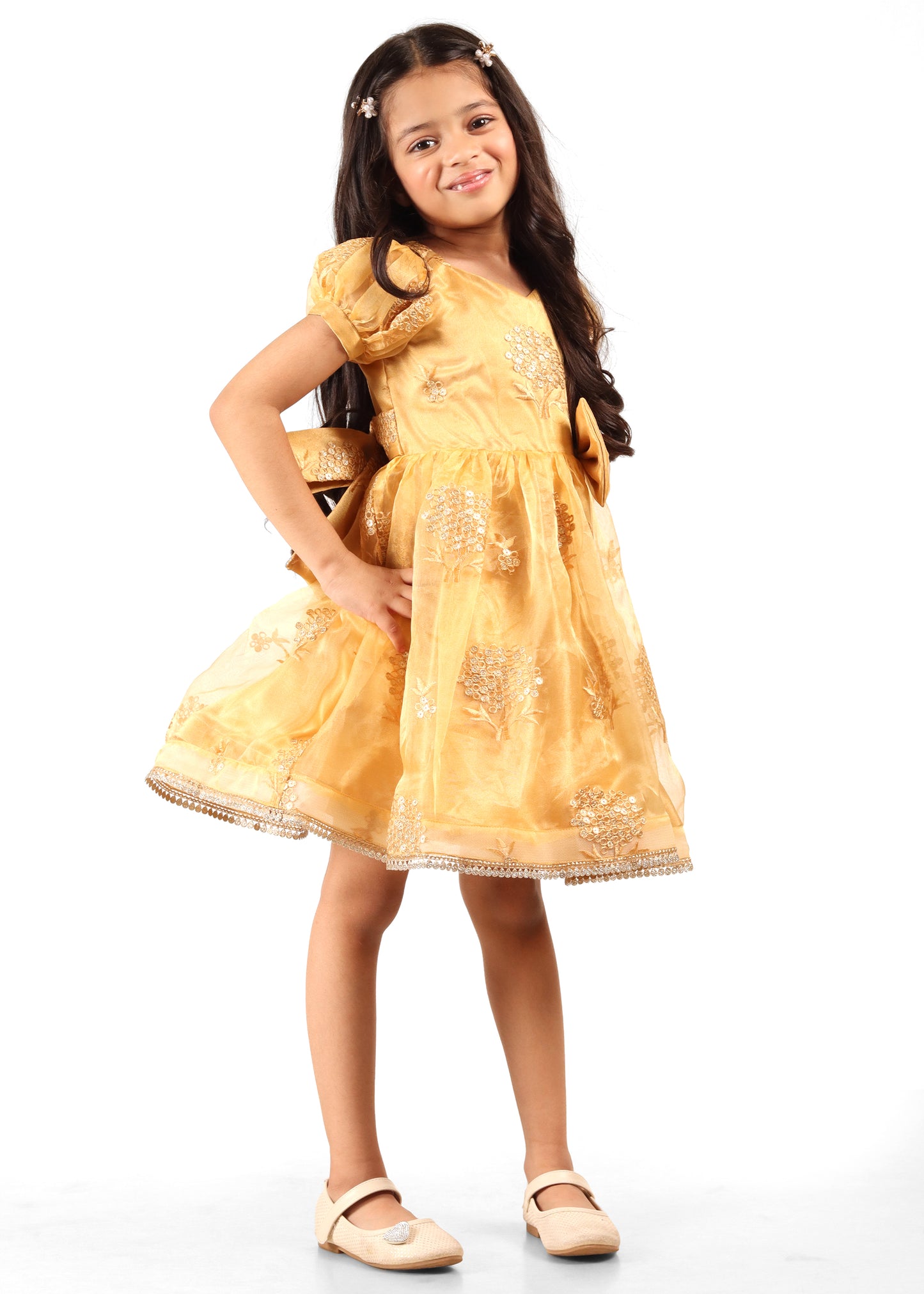 A happy young girl in a golden silk dress embellished with embroidered floral designs, posing for a festive photoshoot.