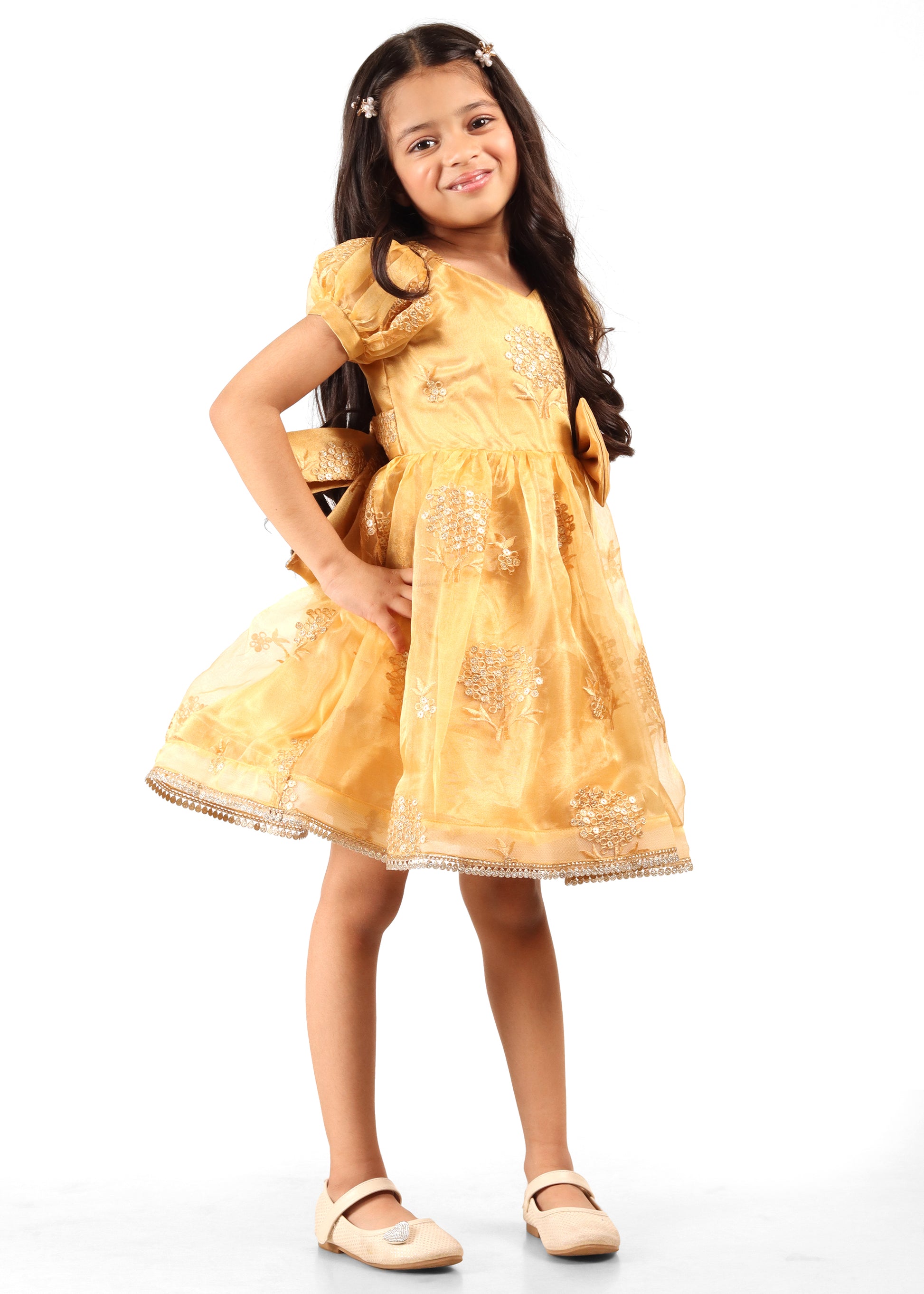 A happy young girl in a golden silk dress embellished with embroidered floral designs, posing for a festive photoshoot.