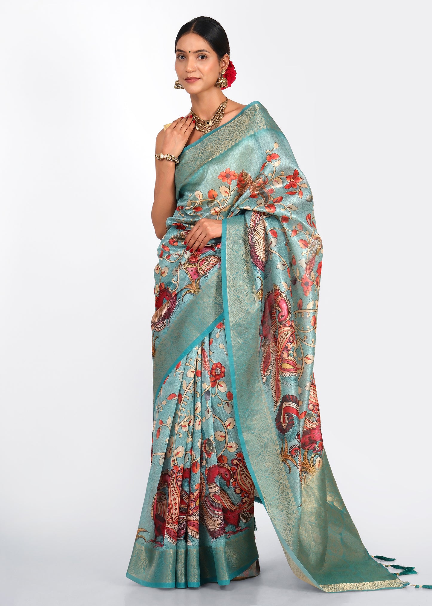 Woman dressed in a teal silk saree with intricate floral and peacock motifs, accessorized with traditional jewelry, exuding elegance and grace.