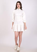 Woman wearing a chic white mini dress with button detailing and flared hem, paired with white sneakers.